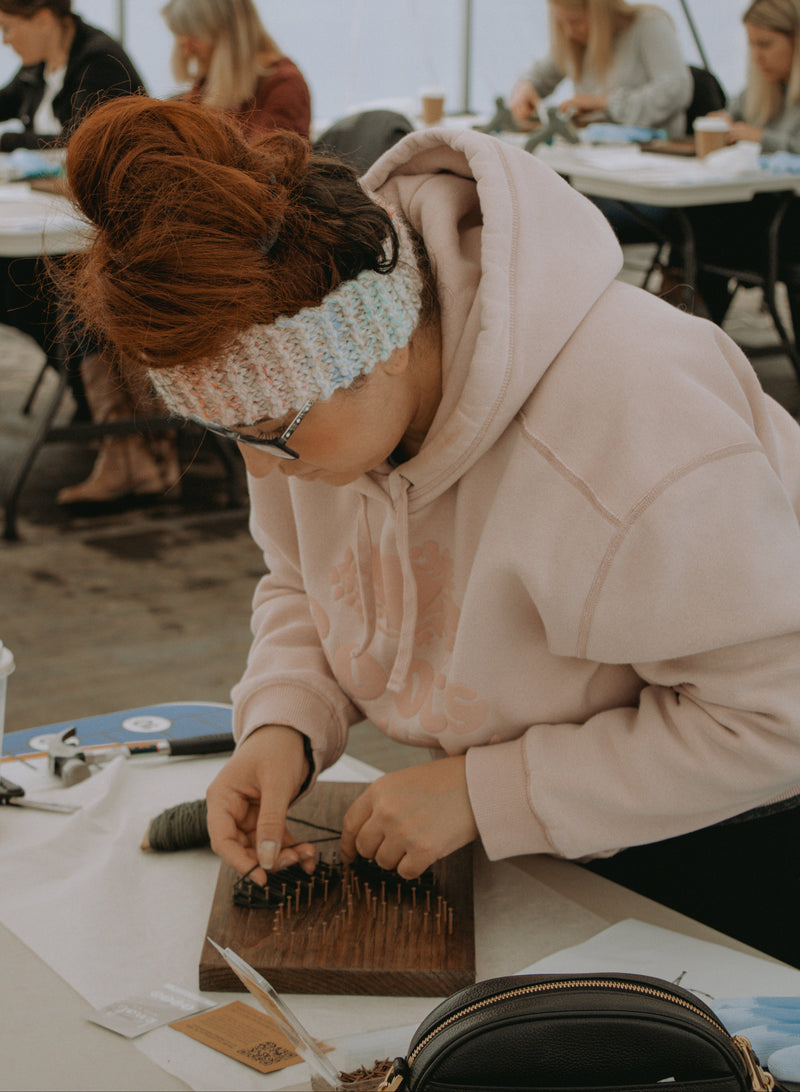 Person working on a craft project at a table with other people in the background.